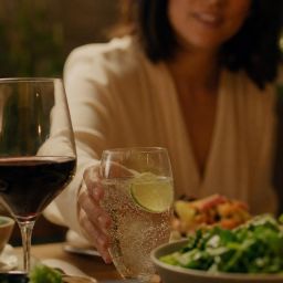 Person choosing sparkling water with lime instead of wine at dinner