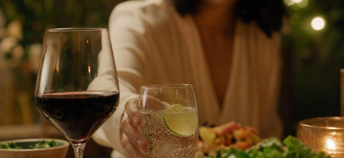 Person choosing sparkling water with lime instead of wine at dinner