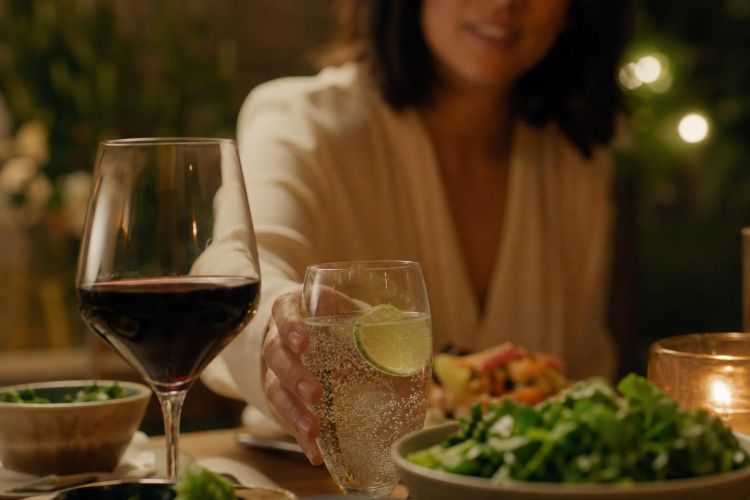 Person choosing sparkling water with lime instead of wine at dinner