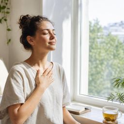 Young woman by a sunny window practicing calm breathing with tea nearby