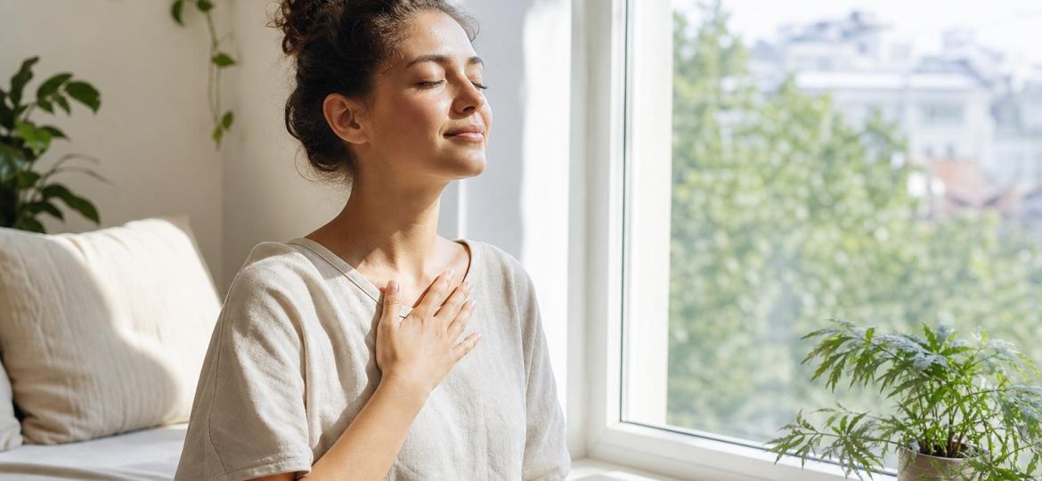 Young woman by a sunny window practicing calm breathing with tea nearby