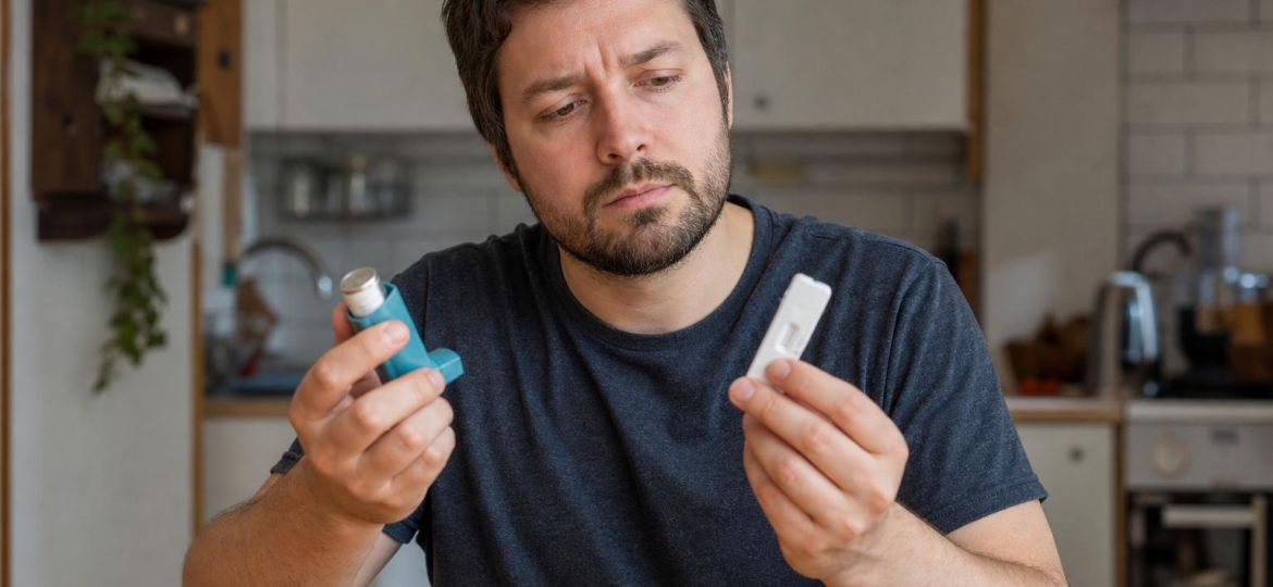 Man holding an asthma inhaler and a rapid test at his kitchen table