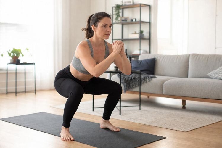 Woman doing a bodyweight squat on a yoga mat in her living room