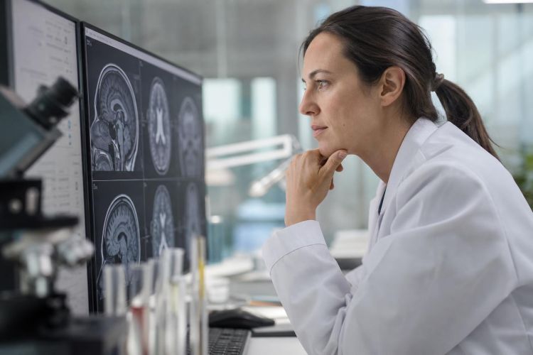 Neuroscientist in a research lab studying a brain MRI scan on a monitor