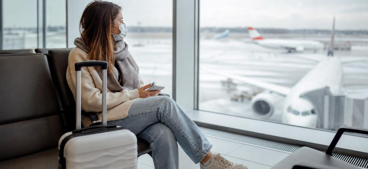 Traveler wearing a face mask in a bright airport terminal with a suitcase