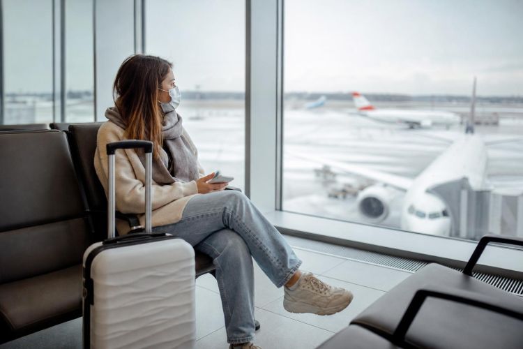 Traveler wearing a face mask in a bright airport terminal with a suitcase