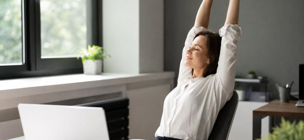 Office worker stretching her arms overhead beside her desk