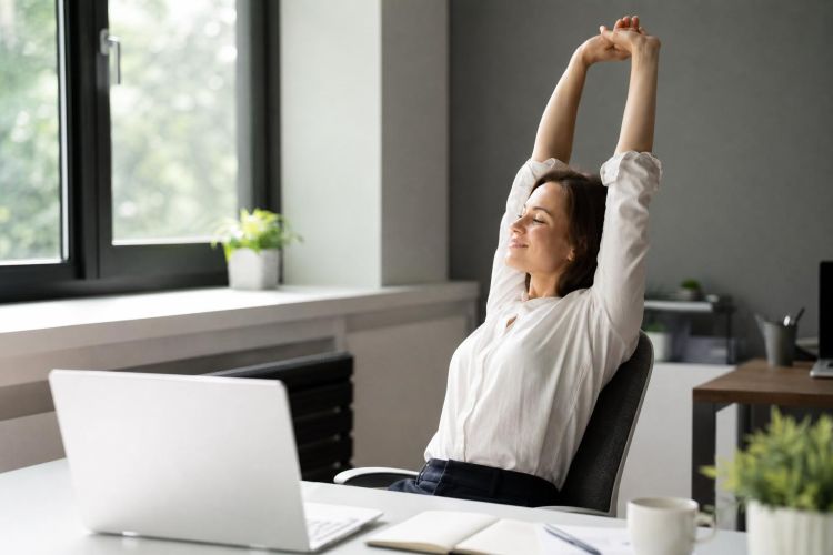 Office worker stretching her arms overhead beside her desk