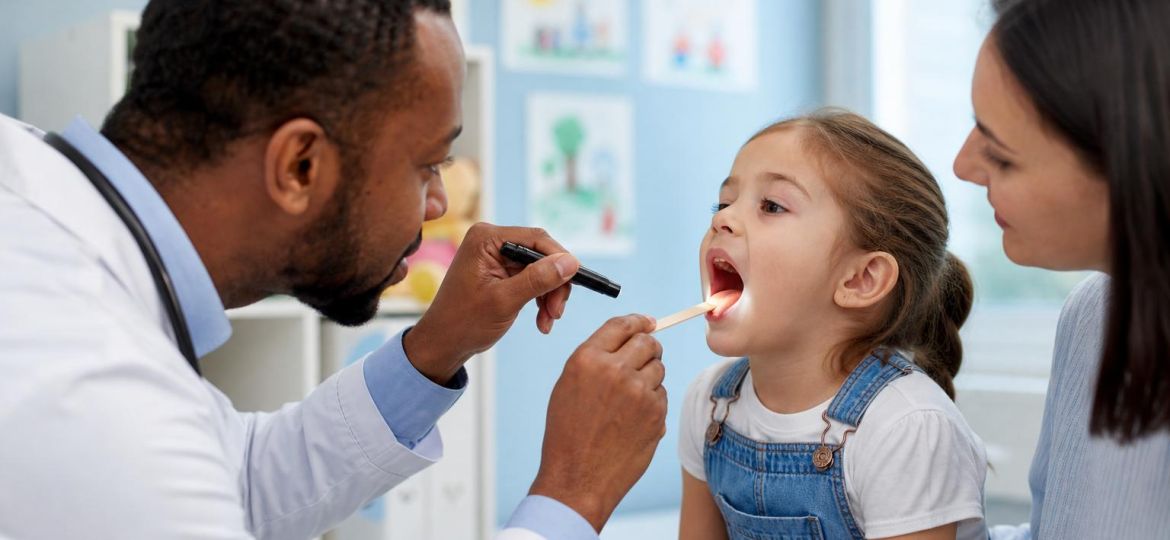 Pediatrician examining a young child's throat with a parent nearby