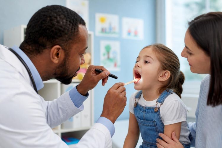 Pediatrician examining a young child's throat with a parent nearby