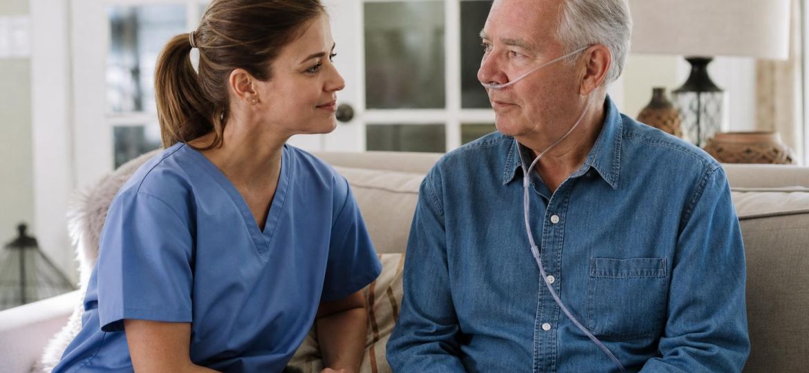 Hospice nurse sitting with an older man using nasal oxygen in his living room