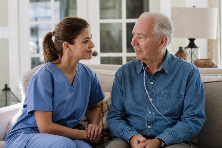 Hospice nurse sitting with an older man using nasal oxygen in his living room