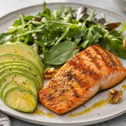 Plate of grilled salmon, avocado, leafy greens, olive oil and walnuts