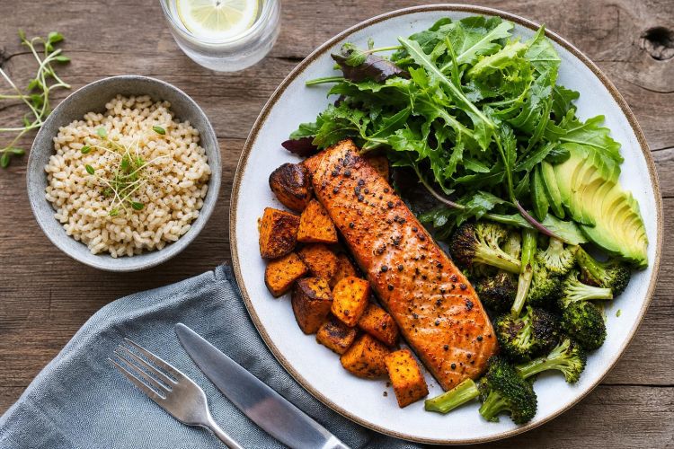 Plate of grilled salmon, avocado, salad and roasted vegetables with a bowl of brown rice