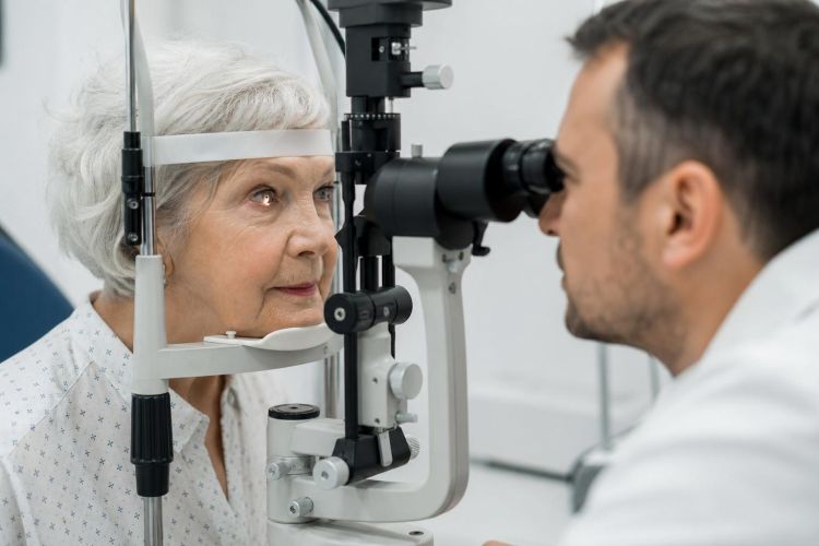 Older woman having an eye exam with an ophthalmologist at a slit-lamp microscope