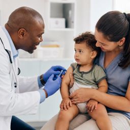 Pediatrician vaccinating a toddler sitting on a parent's lap