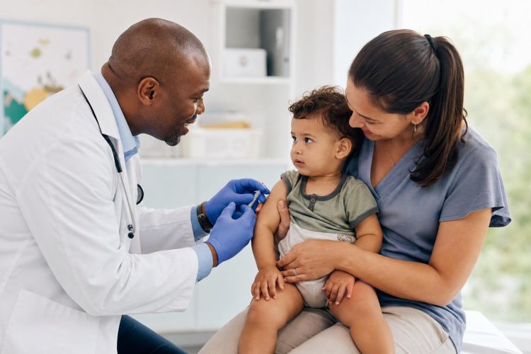 Pediatrician vaccinating a toddler sitting on a parent's lap