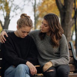 Friend comforting another with an arm around their shoulder on a park bench
