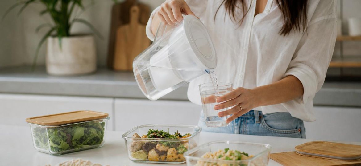 Pouring filtered water from a glass pitcher next to glass food containers