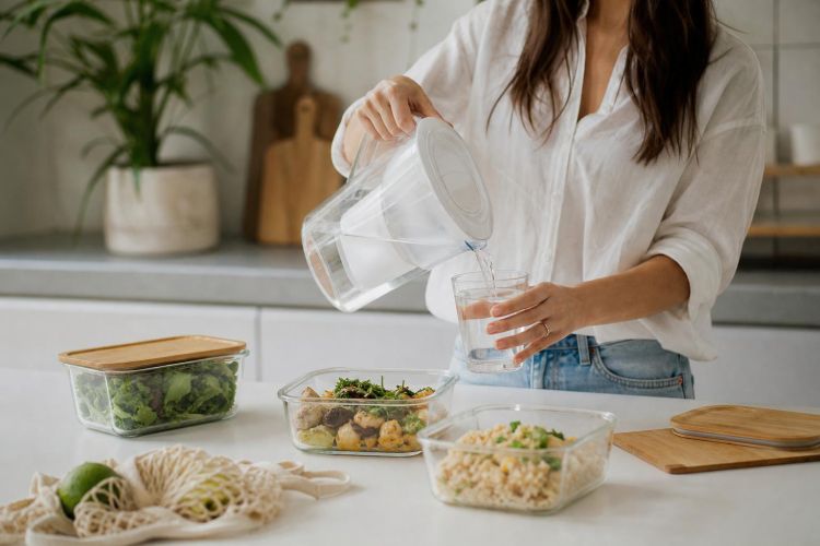 Pouring filtered water from a glass pitcher next to glass food containers