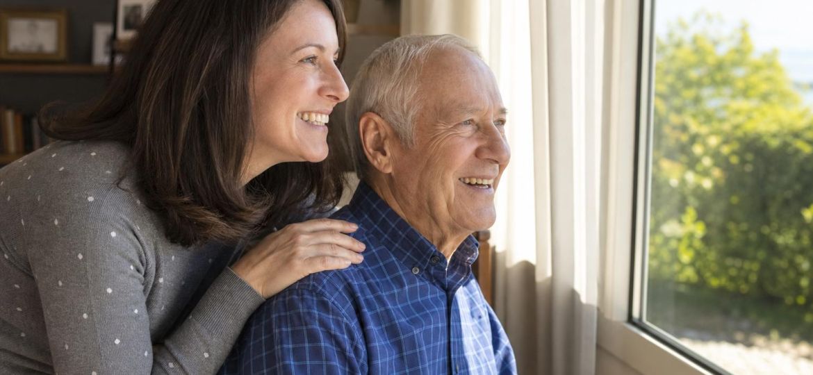 Adult daughter visiting her elderly father by an open sunny window