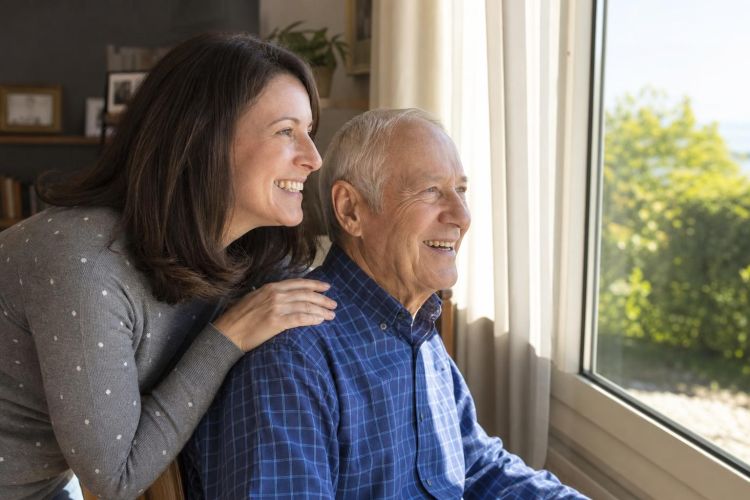 Adult daughter visiting her elderly father by an open sunny window