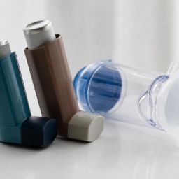 Two asthma inhalers and a spacer on a white table