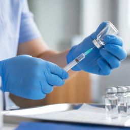 Healthcare worker preparing a vaccine syringe beside small vials on a clinic tray