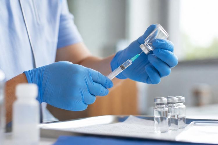 Healthcare worker preparing a vaccine syringe beside small vials on a clinic tray